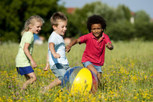 Preschoolers chasing a ball in a field