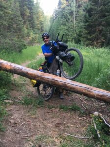 A rider lifting his bike over a fallen tree on the Great Divide