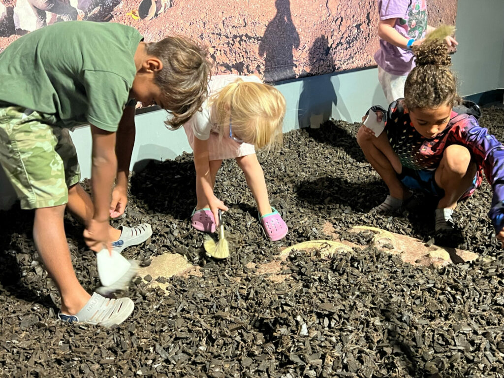 Three children digging for fossils at the Great Lakes Science Center.