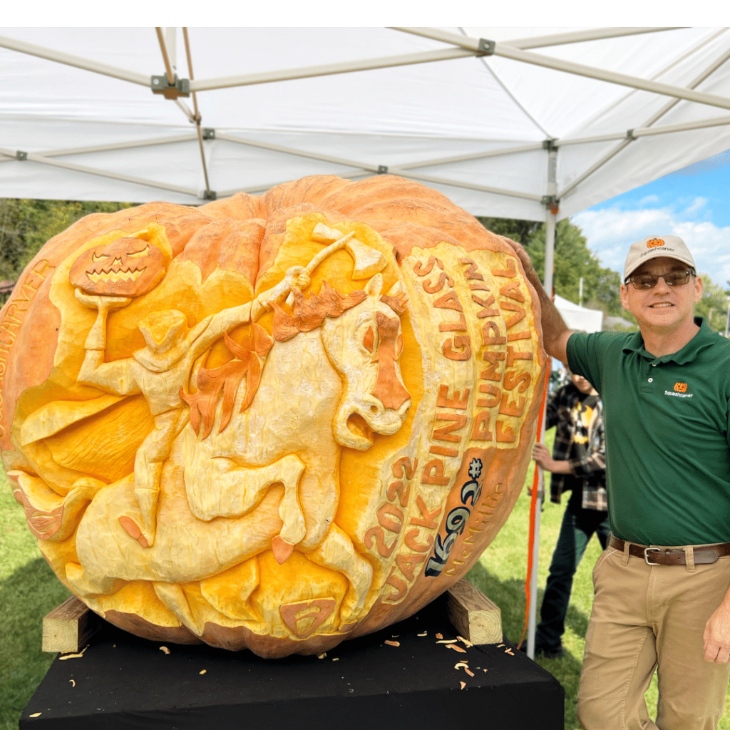 The Squashcarver standing next to his detailed carving of the headless horsemen on a giant pumpkin.
