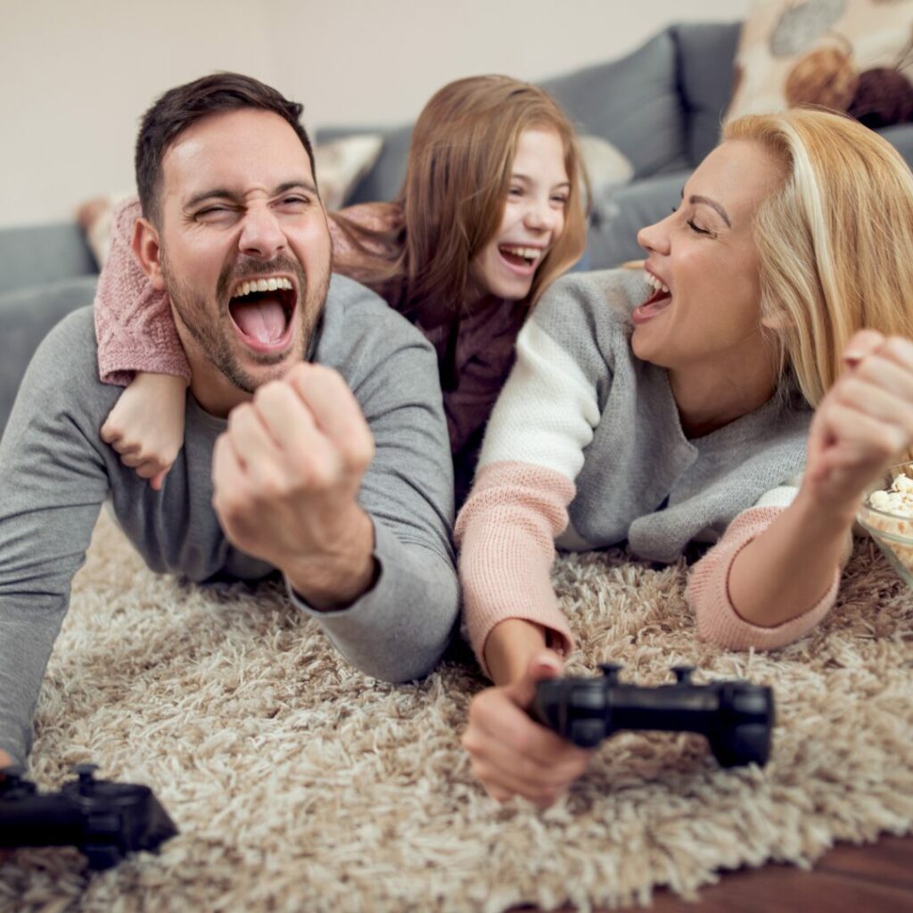 A mom and dad and daughter enjoying the benefits of a 4 day workweek enjoy playing video games together