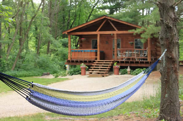 In the background sits cabin in the woods of Hocking Hills and in the forefront is an empty hammock inviting leisure.