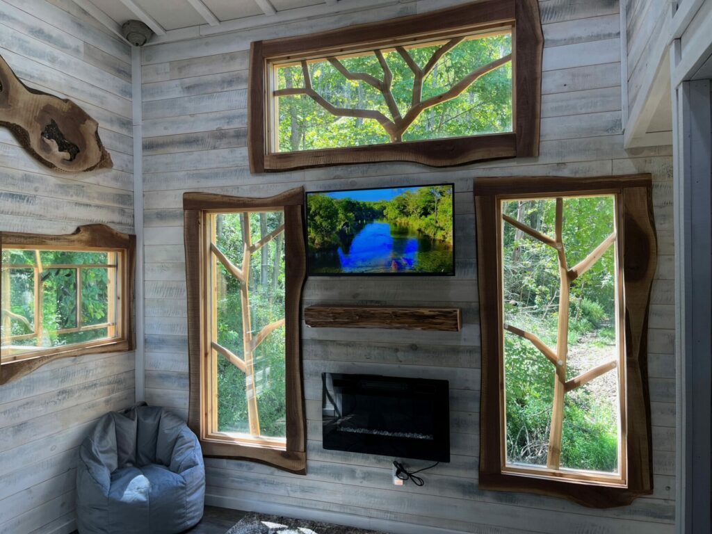An inside view of the treehouses at Owl Hollow featuring the wall with three windows whose panes are adorned with intricate carbed tree branches.