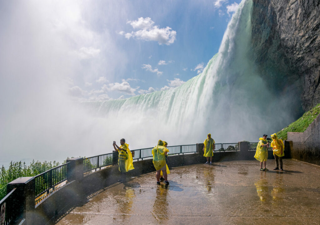 An image of people standing below Niagara Falls and off to the side with mist spraying on them as they are wearing yellow rain coats. 