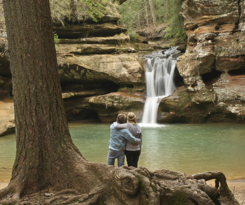 A couple enjoys the cascading water over the rock formations of Hocking Hills