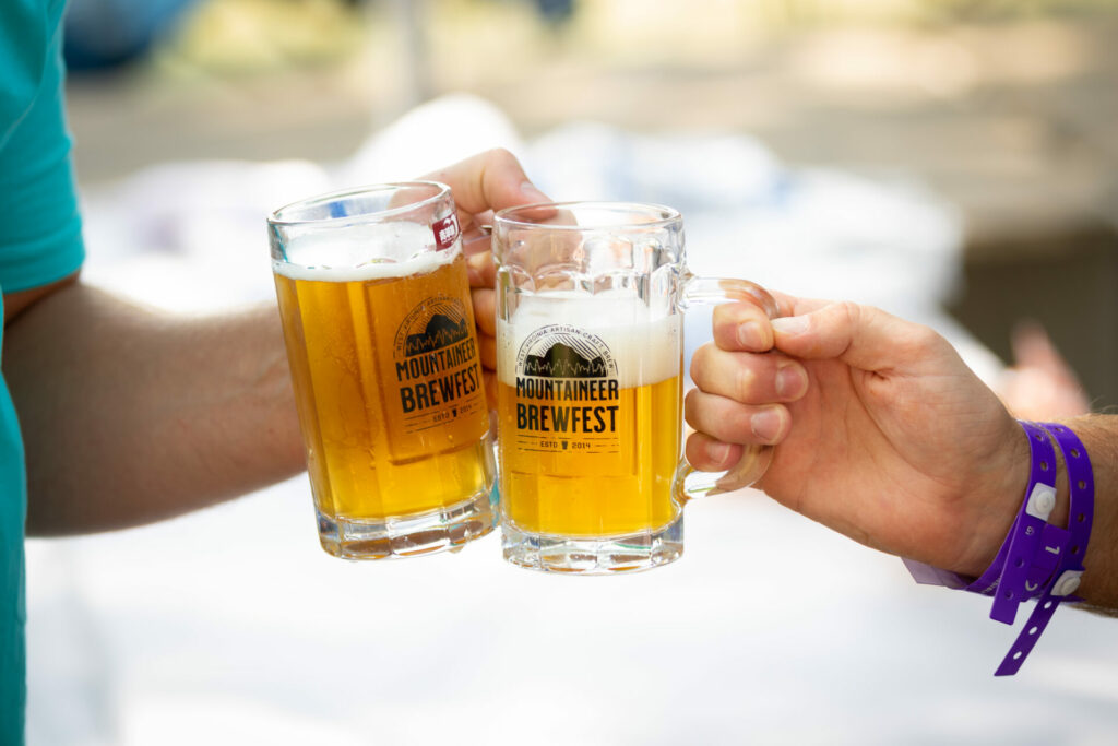 Two extended hands each holding a mug of beer and toasting each other. 