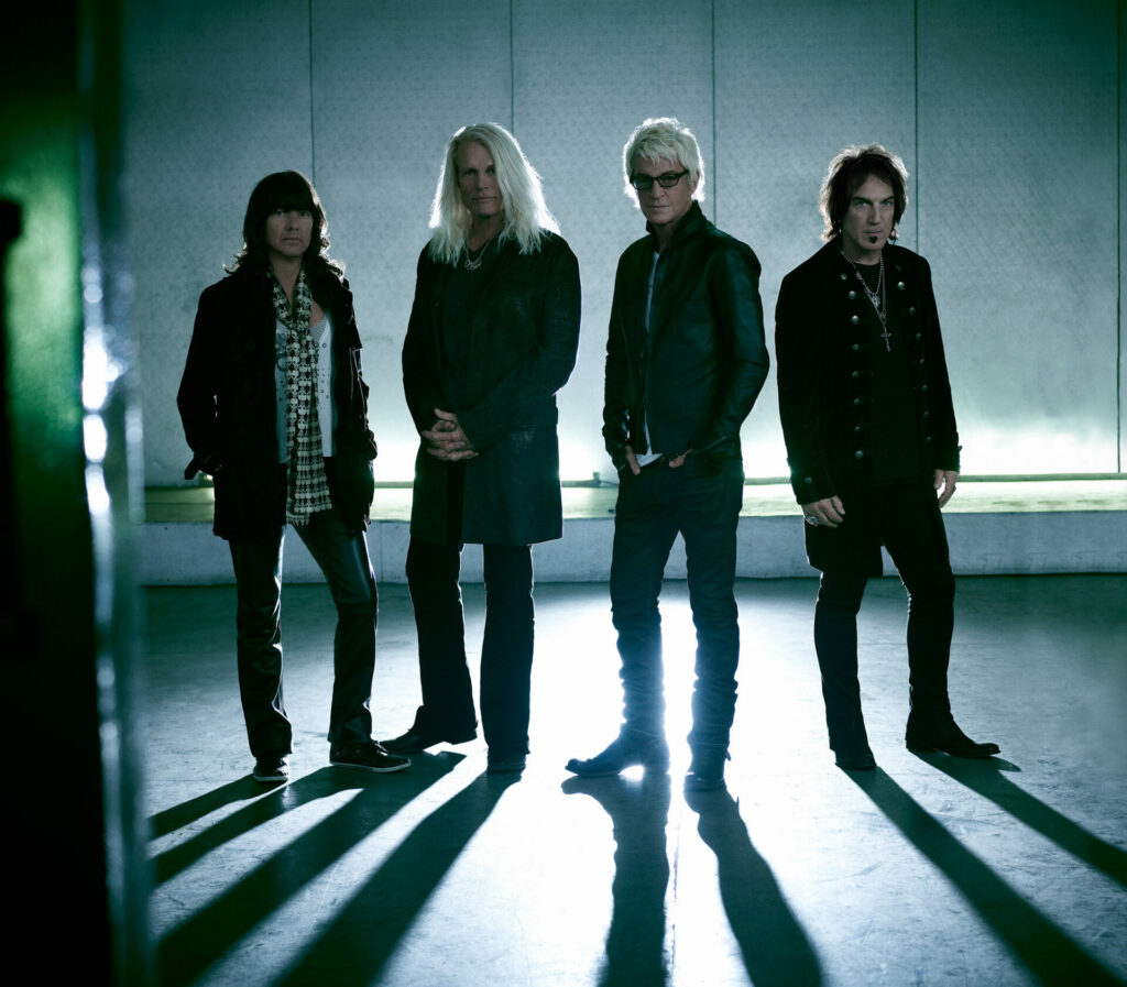 The band REO Speedwagon standing and looking towards the camera backlit with light casting long shadows of the bad in front of them. 