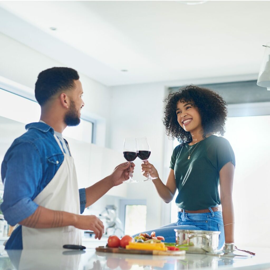 A young couple is sharing a  glass of wine as they cook dinner together for a low-cost date night